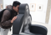 «Sin Censuras»: El desnudo en el arte venezolano rompe tabúes Un joven con mochila y gafas mira curiosamente una escultura interactiva en una galería de arte moderna.