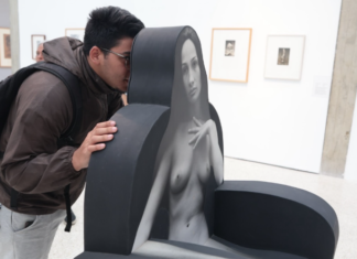 Un joven con mochila y gafas mira curiosamente una escultura interactiva en una galería de arte moderna.