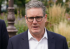 Reino Unido: Renuncia de Keir Starmer Retrato de Keir Starmer, vistiendo un traje azul oscuro y una camisa blanca de cuello abierto, con un fondo desenfocado de un jardín público.