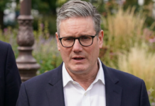 Reino Unido: Renuncia de Keir Starmer Retrato de Keir Starmer, vistiendo un traje azul oscuro y una camisa blanca de cuello abierto, con un fondo desenfocado de un jardín público.